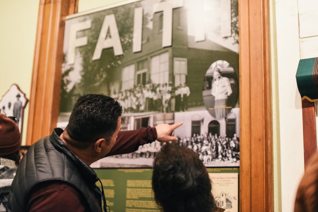 Attendees of Conejos Neighborhood Celebration looking at the exhibit, "Una Familia Grande." They are pointing at a historic photograph.