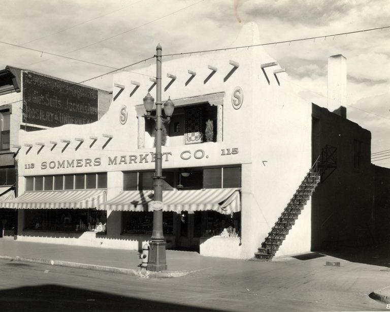 Sommers Market i downtown Colorado Springs on South Tejon that is a three story white stucco structure with protruding logs coming out on the front wall of the store to make it more of an Indian style design. There are multiple windows on each floor with a double door entrance to the market on the right as you walk towards the front entrance to the market.