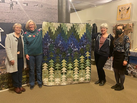 Members of the Quaint Quilters hold up the Sesquicentennial Commemorative quilt that they donated to the CSPM.