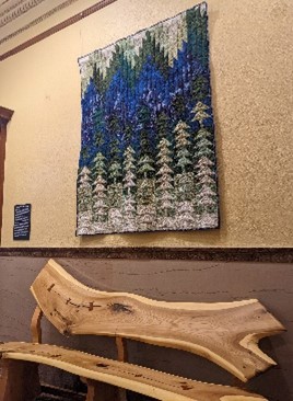 A quilt hangs in the wall in the CSPM above a wood bench.