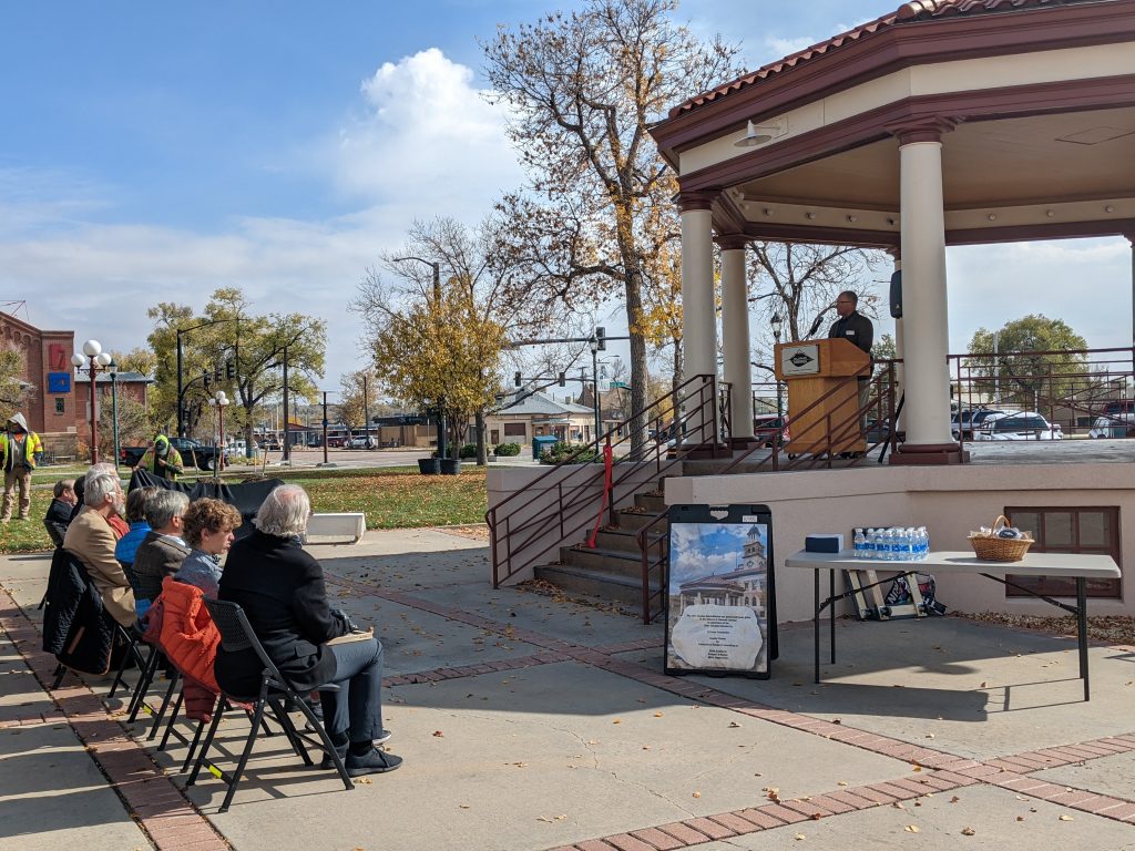 People are seated in front of the CSPM's gazebo where City Forester, Dennis Will, speaks from a lectern.