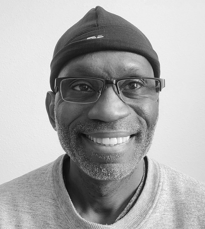 Frank Shines wears glasses and a knit beanie smiles while looking into the camera.