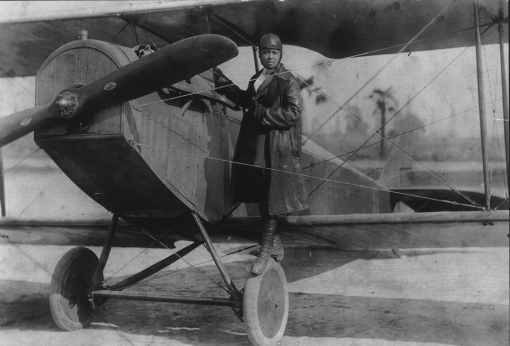 Bessie Coleman stands atop a wing of an airplane.This picture features Bessie Coleman in her JN-4 Curtiss Jenny biplane in 1923. Barred admittance to flying schools in the United States because of her race, she learned to speak French so she could attend flying schools there. She became the first African American woman in the world to receive her pilot’s license. Photo courtesy Wolf Aviation Fund