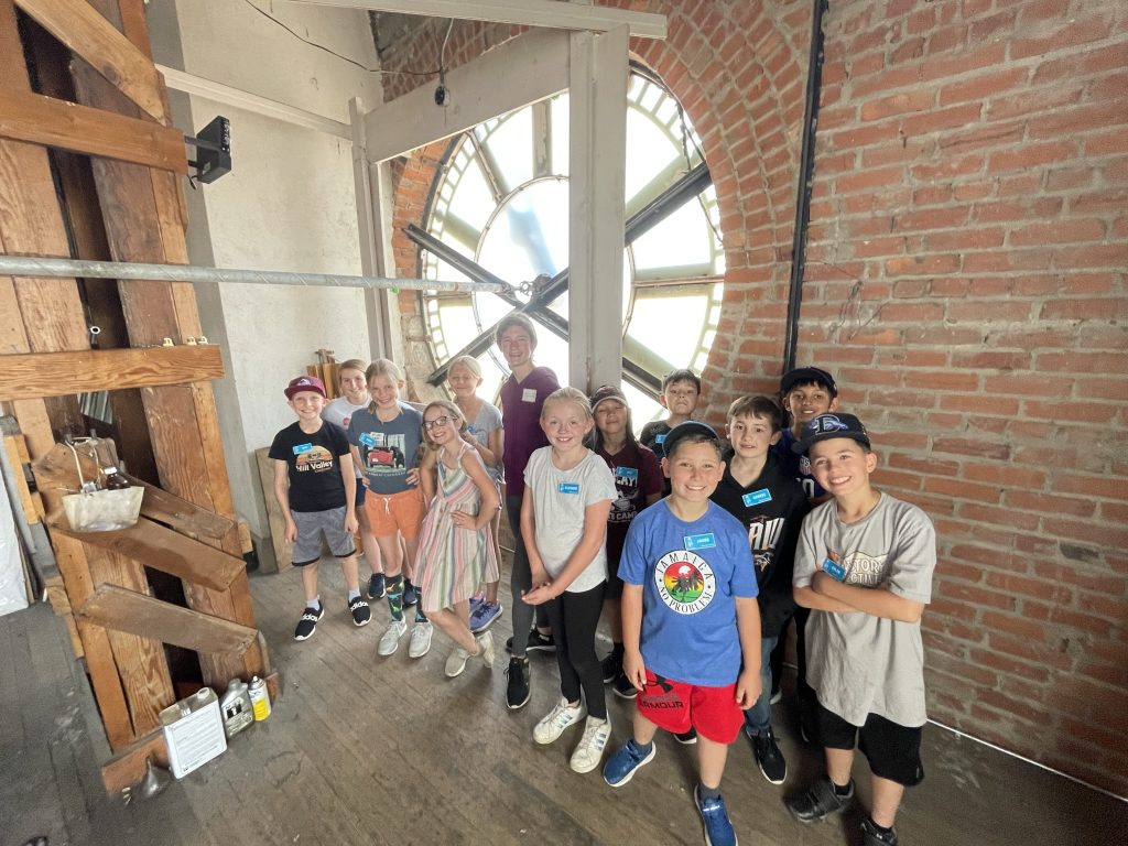 A group of children dressed in summer attire are gathered inside the clocktower of the Colorado Springs Pioneers Museum.