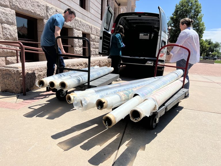 Three individuals moving rugs from the CSPM Collection into a van.