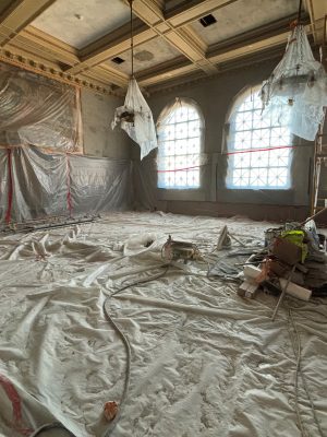 Division III Courtroom currently being rehabilitated into an exhibition gallery space. The room is empty except for plastic sheeting on the floor, the wood paneling and the chandeliers. There is also scaffolding on the right side of the room.
