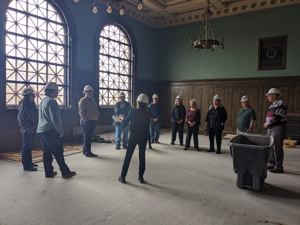 CSPM volunteers on a hard hat tour of the historic 1903 El Paso County Courthouse. A group of ten are standing in the Division III Courtroom looking at the space.