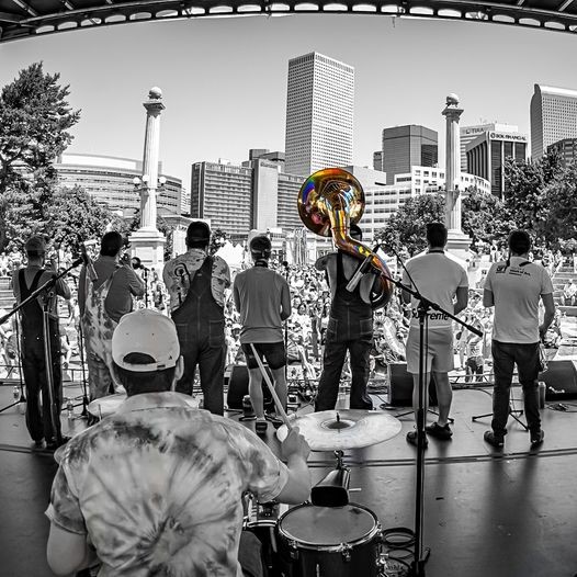 The band Guerilla Fanfare play to a crowd, perspective from behind the band. Edited black and white.