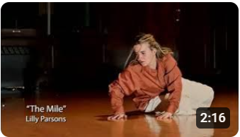Screenshot of the video "The Mile" by Lilly Parsons. The scene is Lilly on laying on the ground propping herself up with two hands.