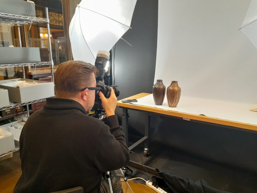 Kenneth Talmadge Stacks is shown here photographing two Van Briggle vases featuring design #653. The bronze-clad vase is part of the CSPM’s Van Briggle Collection, and the copper clad vase belongs to Kathy Honea.